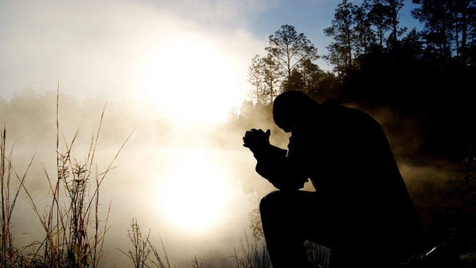 Silhouette praying near a lake.